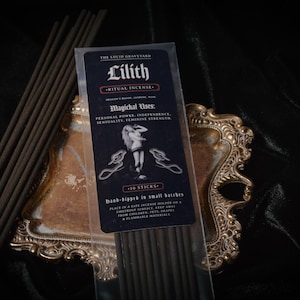 May include: A package of "Lilith Ritual Incense" with a woman illustration, 10 sticks, and text about magical uses. The incense is displayed on a gold-colored ornate tray, with a bundle of incense sticks to the left. The background is dark.