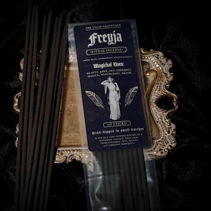 May include: A package of Freyja ritual incense with the text "The Lucid Graveyard" and "Magickal Uses: Beauty, Love, Sex, Fertility, Magick, Witchcraft, Death." The package contains 10 sticks of hand-dipped incense. The incense is dark brown.
