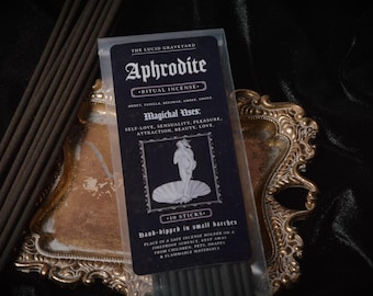 Könnte beinhalten: Eine Packung Aphrodite Ritual-Räucherstäbchen mit einem schwarz-weißen Etikett, präsentiert auf einem goldfarbenen Dekotablett. Das Etikett enthält den Text "Aphrodite", "Ritual Incense" und "Magichal Uses".