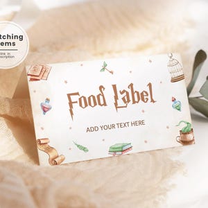 Puede incluir: Etiqueta de comida blanca con un texto marrón "Food Label" y un diseño de rayo. La etiqueta está decorada con ilustraciones de acuarela de una jaula, libros, una botella de poción, un rollo, una llave y una taza de té con una serpiente.