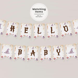 Może przedstawiać: Biało-brązowy baner z napisem "Hello Baby" w brązowych literach. Baner jest ozdobiony obrazkami czarodziejskich kapeluszy, różdżek i innych magicznych przedmiotów.