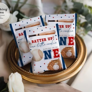 May include: Baseball-themed party favor bags. The bags feature illustrations of a baseball bat, baseball, and glove. Text includes "Batter Up!" and "NE". The bags are decorated with red and blue stars and stripes.
