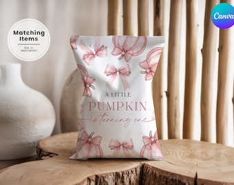 May include: A white party favor bag with pink pumpkins and bows. The bag has the text "A Little Pumpkin is turning one" in pink script. The bag is on a wooden surface.