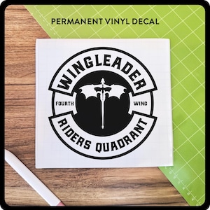May include: A black and white permanent vinyl decal with the text "WINGLEADER" in a circular design. The design includes the words "FOURTH WING" and "RIDERS QUADRANT". A white cutting tool is visible in the image.