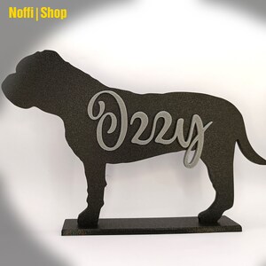 May include: Black silhouette of a dog with the name "Izzy" written in silver on the side. The dog silhouette is standing on a black base.