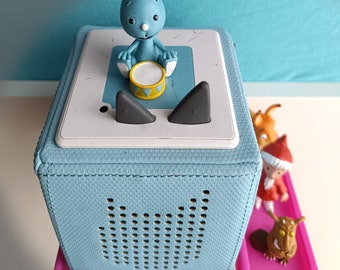May include: A light blue audio player with a white top, featuring a blue bunny figurine playing a yellow drum. The player sits on a pink tray with the text "Valentinas Touchbox". Additional figurines are visible.