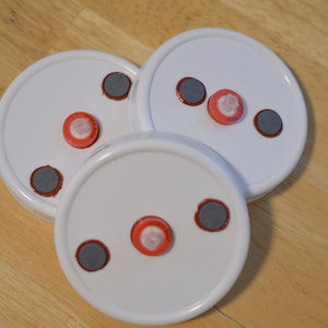May include: Three white round lids with three red and gray circles on each lid.