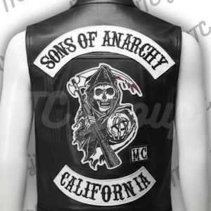 Op de afbeelding: Zwart leren vest met het "Sons of Anarchy" logo op de rug. Het logo bevat een schedel met een zeis en een machinegeweer, met "California" en "MC" patches.