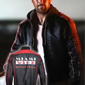 May include: Black and red "Miami Vice Stunt Team" jacket. The jacket has a black body with red accents on the shoulders and sleeves. The text "Miami Vice" is printed on the back in white and blue.