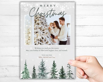 Puede incluir: Una tarjeta de Navidad con una foto de una familia de pie frente a un árbol de Navidad decorado. La tarjeta tiene un fondo blanco con un bosque de acuarela verde en la parte inferior. El texto de la tarjeta dice "Feliz Navidad", "Les deseamos mucha alegría en esta temporada. Que sus vacaciones estén llenas de risas, amor y calidez." y "Los queremos mucho Mike, Michell y Cara."