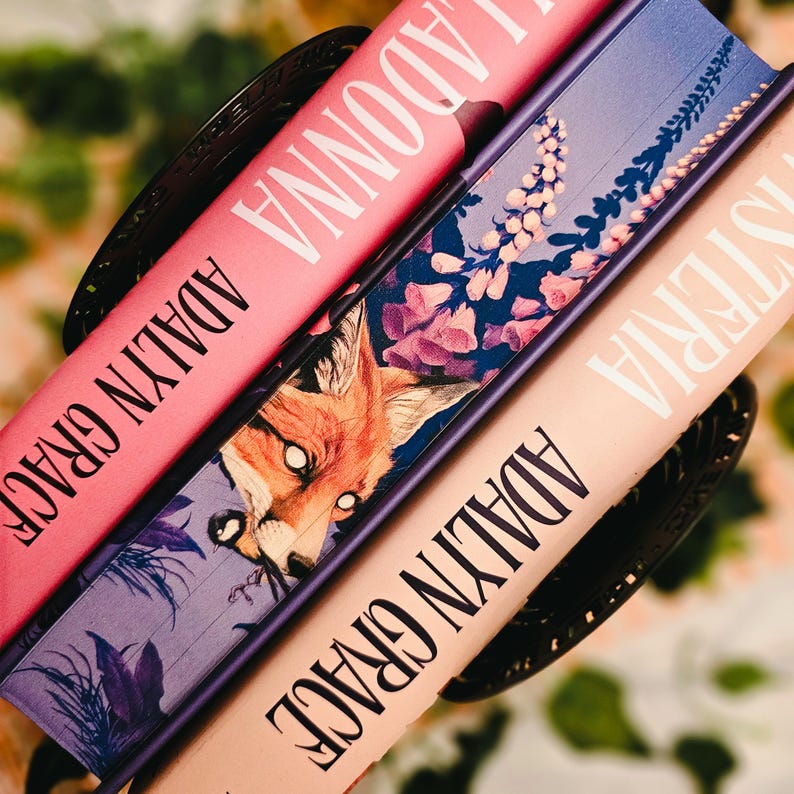 May include: Three hardcover books with the titles "Madonna" and "Hysteria" are stacked. The book spines are pink, lavender, and peach. The middle book features a fox illustration. The author's name, "Adalyn Grace," is printed on each spine.
