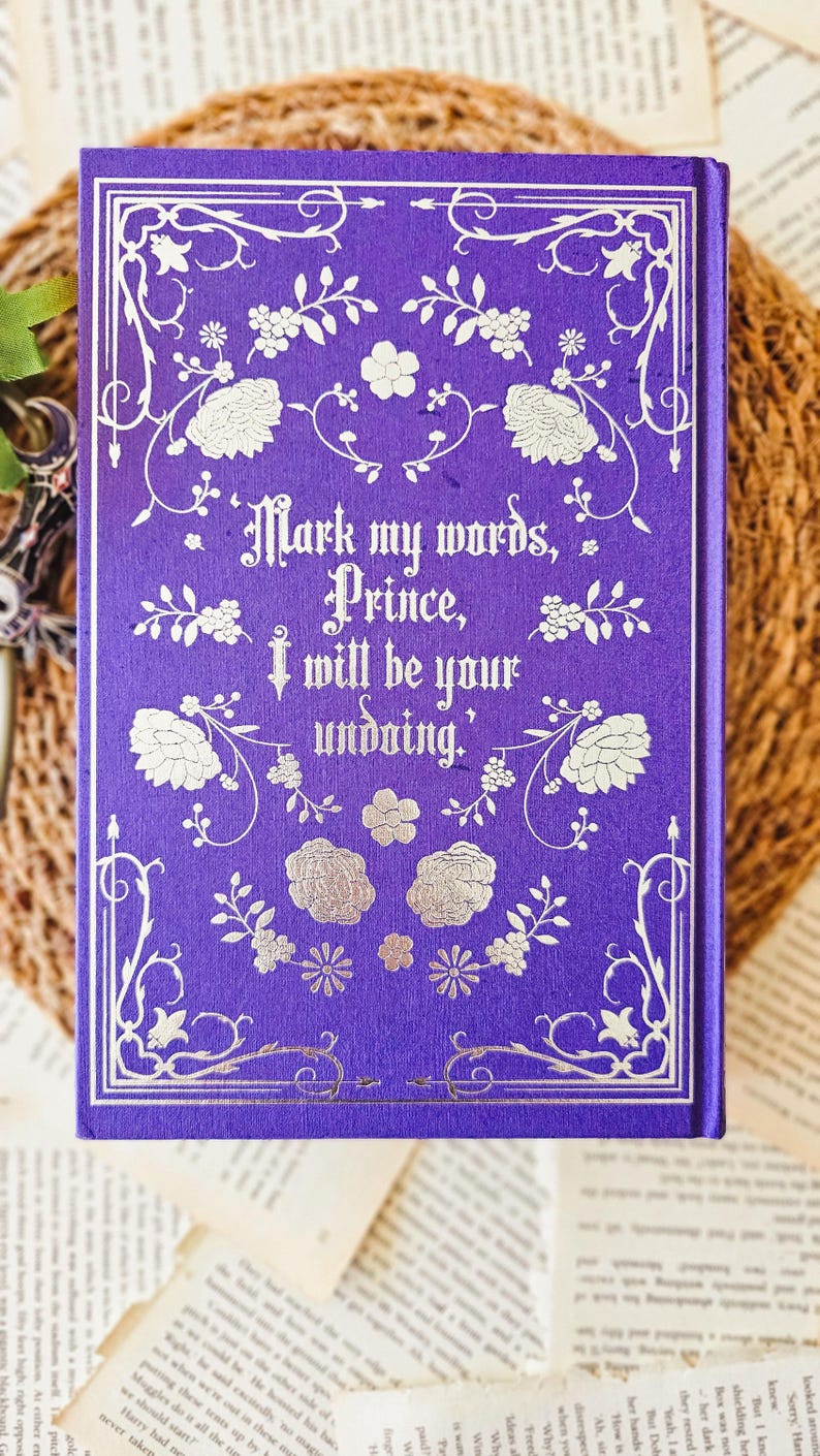 May include: Purple hardcover book with a silver floral design and the text "Mark my words, Prince, I will be your undoing."