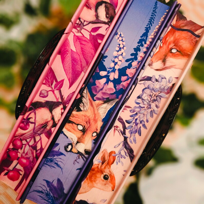 May include: A collection of decorative fans with nature-themed illustrations. The fans feature images of a fox, a squirrel, and floral patterns in shades of pink, purple, and blue. The fans are arranged in a circular pattern, showcasing their detailed artwork.