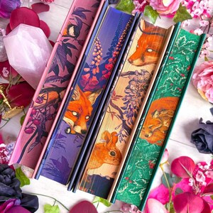 May include: Four decorative books with illustrated covers featuring foxes, flowers, and foliage. The books have pink, purple, tan, and green spines. The image is surrounded by pink and purple flowers.