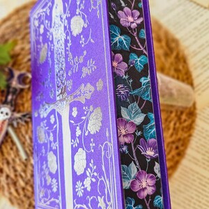May include: A purple hardcover book with a silver floral design and a black and purple floral patterned spine.