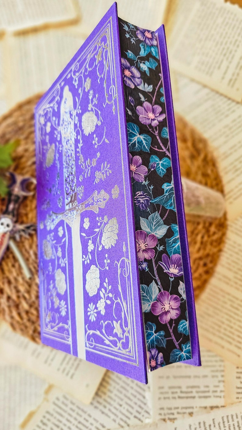 May include: A purple hardcover book with a silver floral design and a black and purple floral patterned spine.