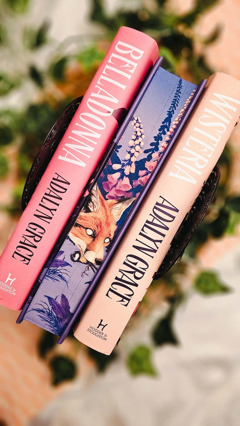 May include: Three hardcover books with titles "Belladonna", "Wisteria", and a third book with a fox illustration. The books are in shades of pink, purple, and peach. The author's name "Adalyn Grace" is printed on the spines.