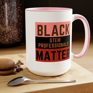 May include: White ceramic mug with a pink rim and handle. The mug features a black, brown, and red graphic that reads "Black STEM Professionals Matter".
