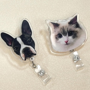 May include: Two clear plastic retractable badge holders. One features a Boston Terrier dog with black and white markings. The other has a Ragdoll cat with blue eyes and gray and white fur. Both have a clear plastic strap and a metal clip.