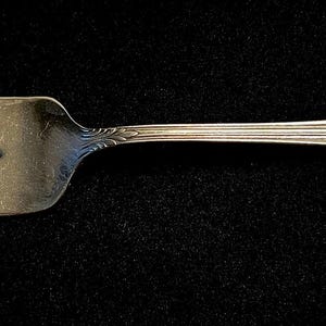 Puede incluir: Tenedor de plata con cuatro púas y un mango decorativo. El mango presenta un diseño floral ornamentado en el extremo. El tenedor está hecho de un metal brillante y reflectante, probablemente plata o una aleación de color plateado. Las púas están espaciadas uniformemente.