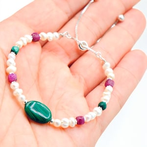 May include: A delicate bracelet featuring white pearls, interspersed with small, vibrant red and green gemstones. A large, oval, polished green stone is the focal point. The adjustable silver chain adds a touch of elegance to this jewelry piece.