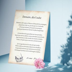 May include: A vintage-style print of a poem by Victor Hugo, "Demain, dès l'aube." The poem is written in French and is about a person leaving to see someone they love. The print is on aged paper with a brown background and is decorated with a drawing of books and a pen.