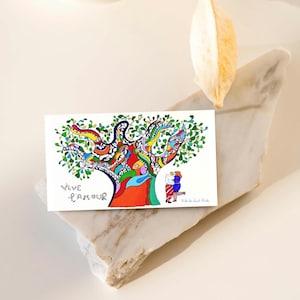 Puede incluir: Una colorida impresión artística que presenta un árbol vibrante con un tronco multicolor y hojas verdes. Las palabras "Vive L'Amour" están escritas en escritura negra. Dos figuras se abrazan bajo el árbol. Una pieza decorativa.
