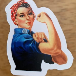 Può includere: Un adesivo in stile vintage con una donna con un bandana rosso e bianco a pois, che flette il bicipite. Indossa una camicia blu e ha un'espressione determinata sul viso.