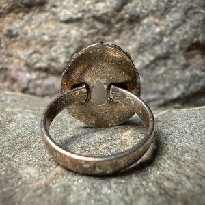 A silver ring with a pendant is resting on a rock surface.