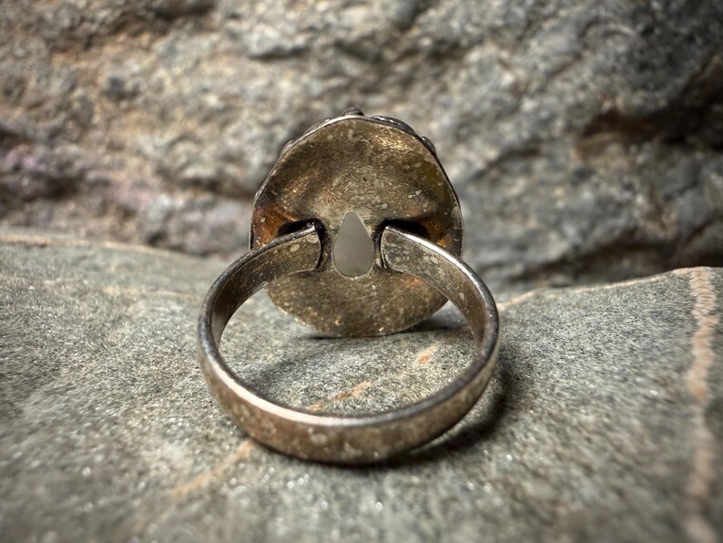 A silver ring with a pendant is resting on a rock surface.