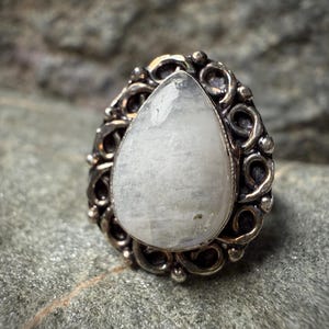 A close-up image of a white stone or gemstone, possibly a pearl or crystal, set in an ornate metal ring or pendant.