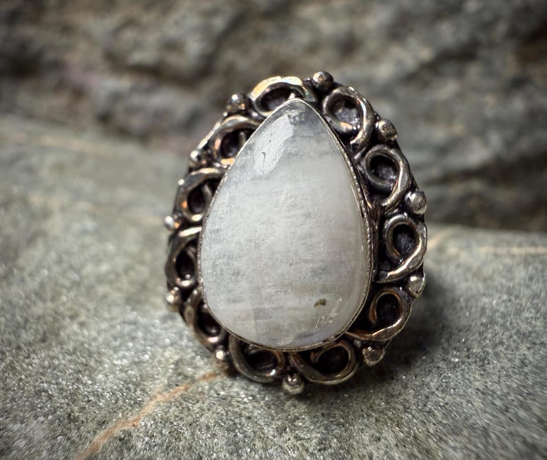 A close-up image of a white stone or gemstone, possibly a pearl or crystal, set in an ornate metal ring or pendant.