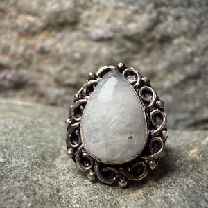 A close-up image of a white stone or gemstone, possibly a pearl or a crystal, set in an ornate metal ring or pendant.