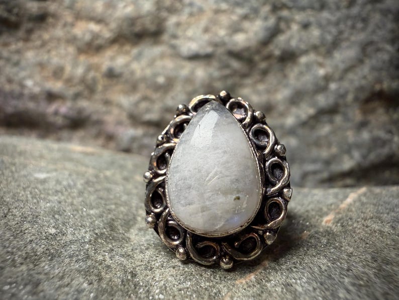 A close-up image of a white stone or gemstone, possibly a pearl or a crystal, set in an ornate metal ring or pendant.