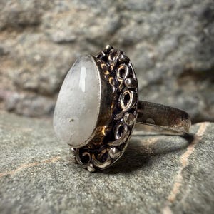 A silver ring with a large white stone sits on a gray rock.