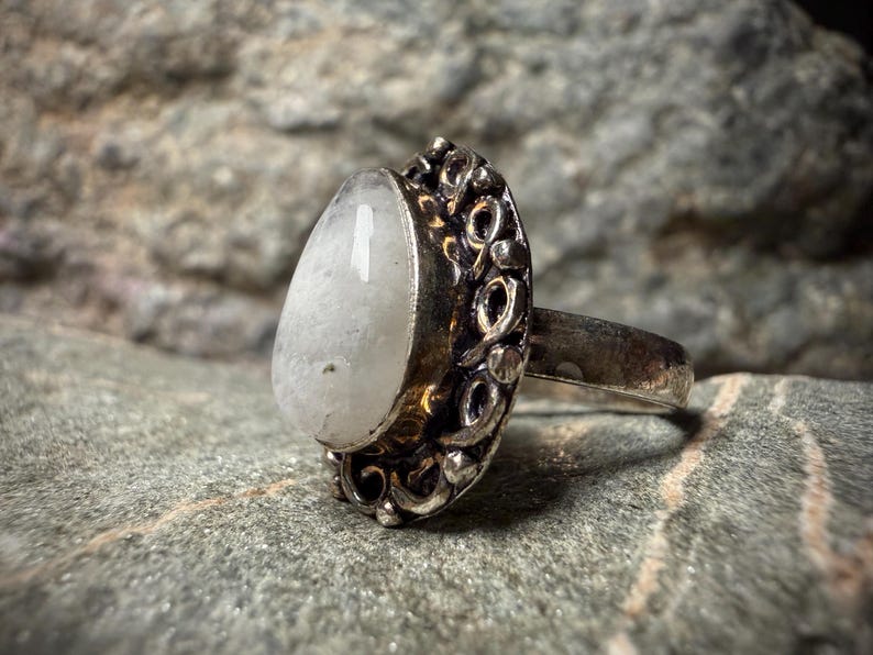 A silver ring with a large white stone sits on a gray rock.