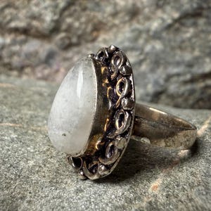A silver ring with a large, white stone or gemstone in the center, set in an ornate, decorative metal band.