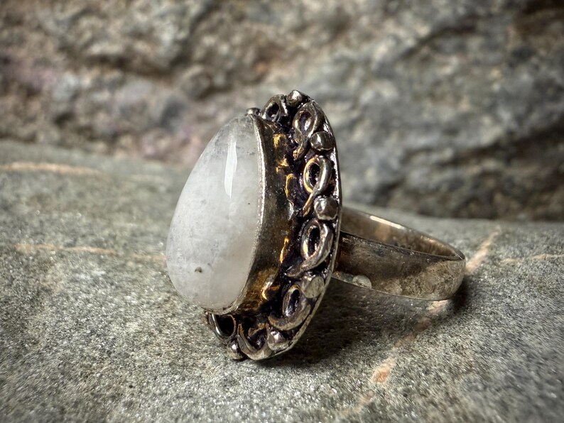 A silver ring with a large, white stone or gemstone in the center, set in an ornate, decorative metal band.