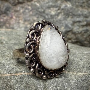 A silver ring with a large, white gemstone, possibly a moonstone, set in an ornate, decorative metal frame.