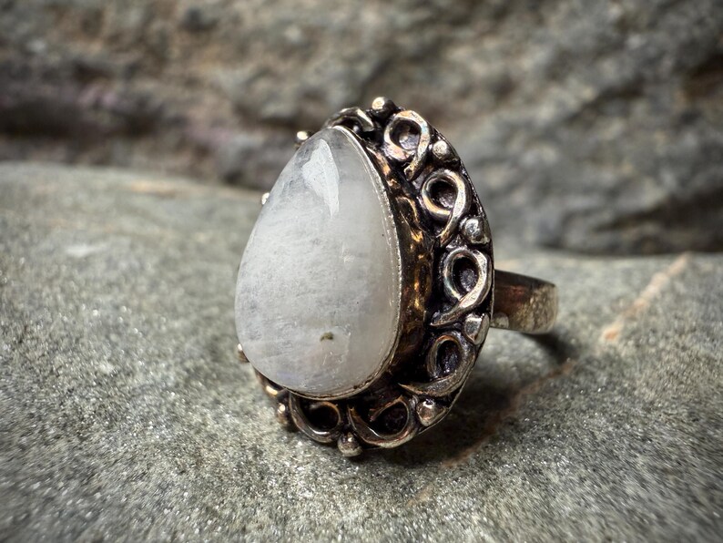 A silver ring with a large, white stone or gemstone in the center, surrounded by an intricate, decorative metal frame.