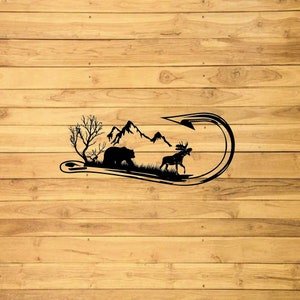 May include: Black silhouette of a bear, moose, and mountain range inside a fish hook. The design is on a wood background.