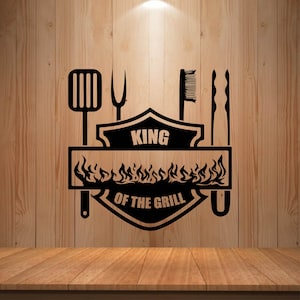 May include: Black and white graphic design with the text "King of the Grill" in a shield shape with flames. The design includes a spatula, fork, grill brush, and tongs.