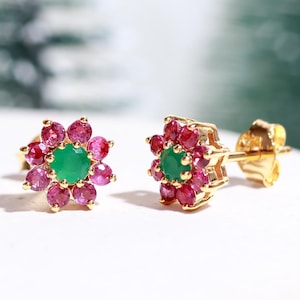 Puede incluir: Un par de pendientes de oro con una piedra preciosa verde redonda central rodeada por un halo de ocho pequeños rubíes rosas redondos, dispuestos en un patrón floral con un poste y un cierre de metal seguro para el lóbulo de la oreja.