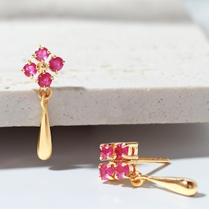 Pode incluir: Um par de brincos de ouro com um grupo de quatro pedras preciosas rosa redondas dispostas em um padrão quadrado, com um pingente de ouro liso e polido em forma de gota pendurado na base de cada pino de brinco.