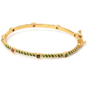 Op de afbeelding: Een goudkleurige scharnierende armband met een gedraaid touwontwerp en groene emaille details. De armband is versierd met kleine, ronde, veelkleurige edelstenen die met tussenpozen langs de band zijn geplaatst en heeft een metalen sluiting.