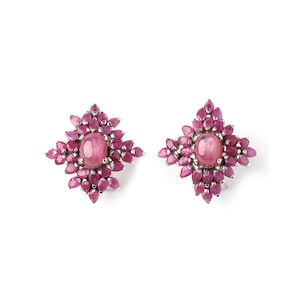 May include: A pair of earrings featuring a central oval pink gemstone surrounded by smaller, teardrop-shaped pink gemstones. The earrings have a silver-colored metal setting and a floral design. The background is plain white.