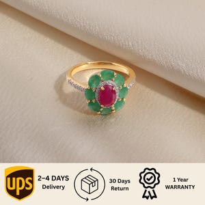 Op de afbeelding: Een gouden ring met een centrale ovaal geslepen rode robijn omringd door een halo van ronde groene smaragden. De ringband is gemaakt van goud en bevat kleine witte accentstenen langs de zijkanten, wat zorgt voor een bloemmotief.