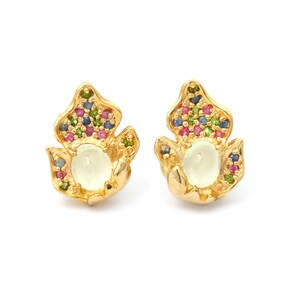 May include: A pair of gold-coloured earrings. Each earring has a central oval, pale yellow stone, surrounded by small, colourful gemstones in pink, green, blue, and purple. The earrings are designed with a floral motif.