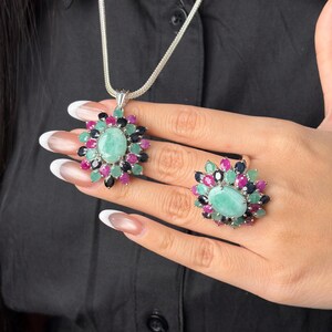 Puede incluir: Un conjunto de collar con colgante y anillo de plata. La joyer&iacute;a presenta una gema grande, ovalada, de color verde claro, rodeada de gemas m&aacute;s peque&ntilde;as en rosa, verde y negro. El collar tiene una cadena de plata.