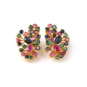 May include: A pair of gold-toned earrings, each adorned with an array of colorful gemstones. The gemstones include ruby, emerald, sapphire, and other stones in shades of pink, green, and blue. The earrings have a cluster design.